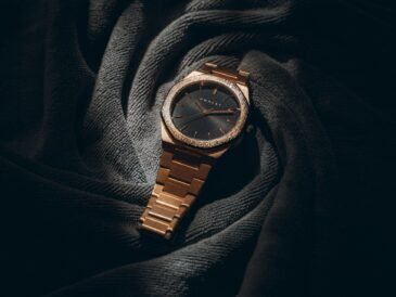 a rose gold watch resting on dark fabric