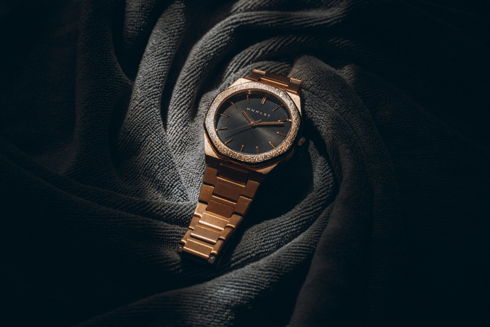 a rose gold watch resting on dark fabric